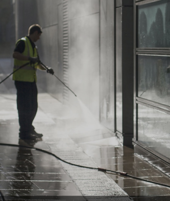 Worker pressure washing a building exterior with visible steam and spray