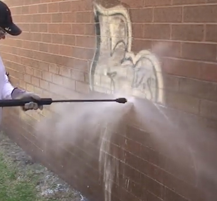 Person pressure washing graffiti off a brick wall